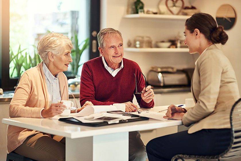 Couple de personnes âgées discutant avec une conseillère autour d’une table, examinant des documents relatifs à l’hébergement ou aux services pour aînés.